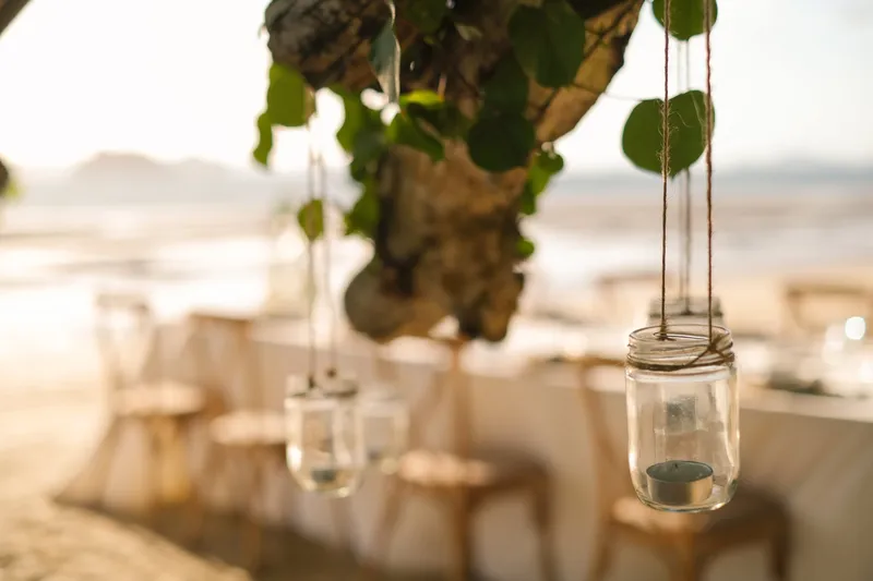 Long outdoor dinner table set by the ocean with hanging candle jars