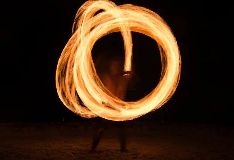 Fire performer spinning flames on a beach at night